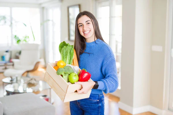 Mujer joven sonriendo sosteniendo una caja de madera de comestibles de deliv —  Fotos de Stock