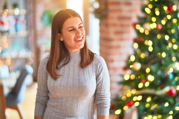 クリスマスツリーの周りに幸せな顔をして立って若い美しい女性とお祝いのために笑顔を提示 — ストック写真
