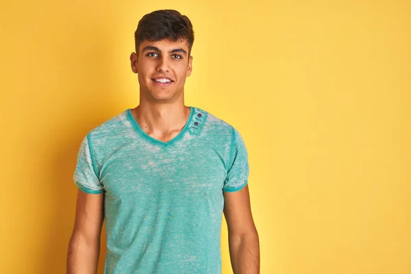 若いインド人男性の顔に幸せとクールな笑顔で孤立した黄色の背景の上に立って緑のTシャツを着て 運のいい人 — ストック写真