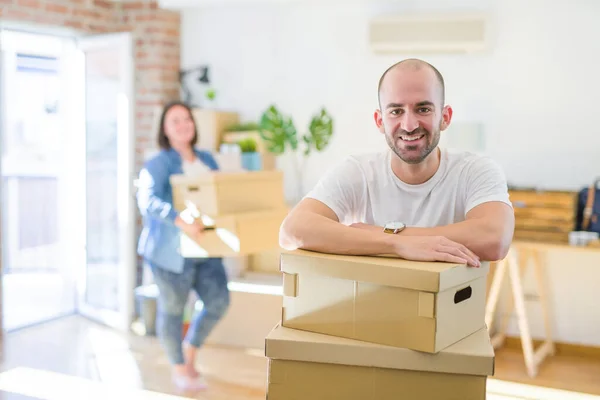 Young couple moving to new apartment, handsome man leaning on cardboard boxes and smiling happy