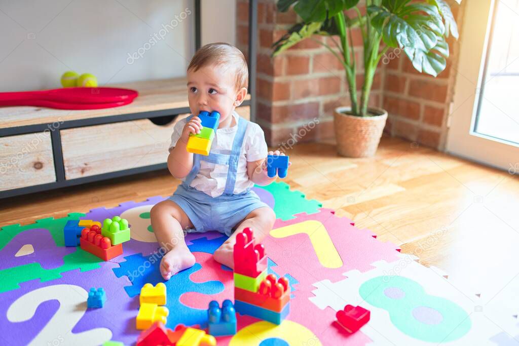 Beautiful toddler sitting on puzzle carpet playing with building blocks at kindergarten