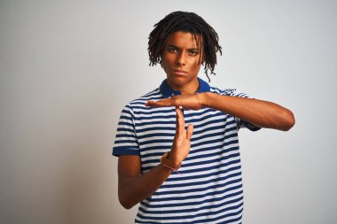 Afro man with dreadlocks wearing striped blue polo standing over isolated white background Doing time out gesture with hands, frustrated and serious face