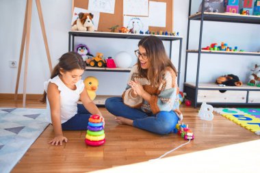 Anaokulundaki bir sürü oyuncağın etrafında çemberler kullanarak piramit inşa eden güzel öğretmen ve bebek.