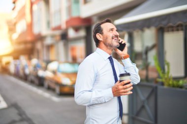 Orta yaşlı yakışıklı işadamı akıllı telefondan konuşuyor. İçiyor, kahveyi götürüyor, gülümsüyor.