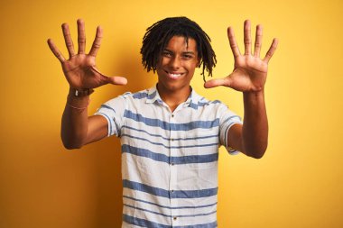 Sarı arka plan üzerinde çizgili gömlek giyen Afro-Amerikalı bir adam 10 numarayı gösterirken kendinden emin ve mutlu bir şekilde gülümsüyor..