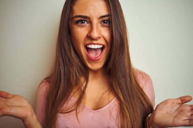 Pembe tişörtlü genç bir kadın izole edilmiş beyaz arka planda mutlu ve heyecanlı duruyor. Kazanan yüz ifadesi zaferi büyük bir gülümsemeyle kutluyor.