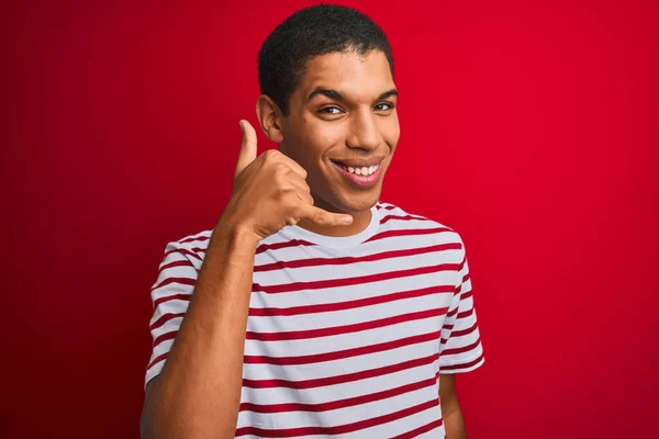 年轻英俊的阿拉伯男子穿着条纹T恤 披着孤立的红色背景 微笑着 用手和手指做着电话手势 就像在电话里说话一样 交流概念 — 图库照片