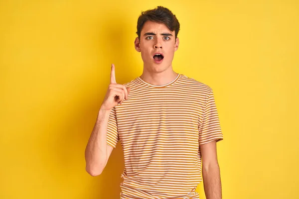Teenager boy wearing yellow t-shirt over isolated background pointing finger up with successful idea. Exited and happy. Number one.