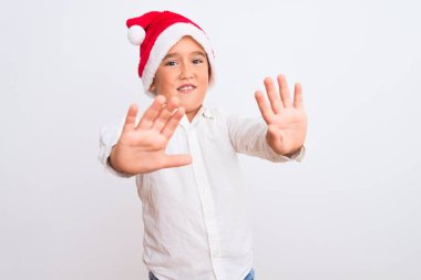 Noel Baba şapkası takan güzel çocuk beyaz arka plan üzerinde korkmuş ve korkudan dehşete düşmüş halde duruyor. El hareketlerini durdur, şok içinde bağır. Panik konsepti.