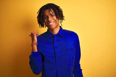 Sarı arka plan üzerinde mekanik üniforma giyen Afro işçi. Gülümsüyor ve baş parmağıyla yüzünü gösteriyor..