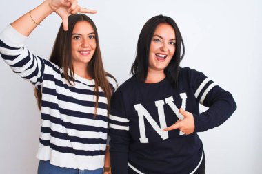 İzole edilmiş beyaz arka planda sıradan kıyafetler giyen genç ve güzel kadınlar gülümseyerek mutlu yüzlü elleri ve parmakları olan bir çerçeve yapıyorlar. Yaratıcılık ve fotoğrafçılık kavramı.