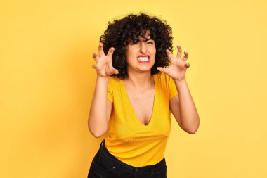 Sarı arka planda duran kıvırcık tişörtlü, kıvırcık saçlı genç Arap kadın kedi gibi gülüyor, agresif ve seksi bir ifade takınıyor.