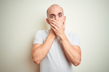 Sakallı genç ve kel bir adam izole edilmiş arka planda günlük beyaz tişört giyiyordu. Ağzını yanlışlıkla ellerle kapatarak şok etti. Gizli konsept.