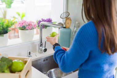 Genç kadın lavabo su kullanarak sebze ve meyve yıkama