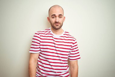 Sakallı genç ve kel bir adam beyaz izole edilmiş arka plan üzerine sıradan kırmızı tişört giyiyor. Uykulu ve yorgun görünüyor. Yorgunluktan ve akşamdan kalmalıktan yorgun ve tembel gözlerle bakıyor..