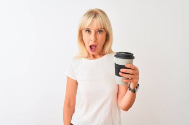 Orta yaşlı bir kadın izole edilmiş beyaz arka planda duran kahve kadehini içerken şaşkınlık dolu bir yüzle korkmuş ve korku ifadesinden heyecanlanmış.