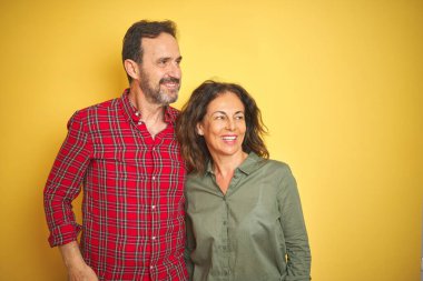 Güzel orta yaşlı çift, izole edilmiş sarı arka planda. Yüzlerinde gülümseme, doğal bir ifade ile yan yana bakıyorlar. Kendinden emin gülen.