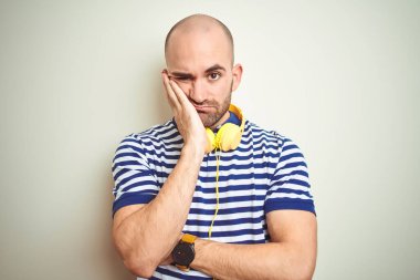Sarı kulaklık takıp müzik dinleyen genç adam kollarını kavuşturup depresyondan sıkılmış ve yorgun görünüyor..