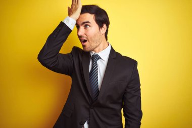 Takım elbiseli ve kravatlı genç yakışıklı bir işadamı, izole edilmiş sarı arka planda dikilirken, yanlışlıkla el ele tutuşarak şaşırdı. Hatayı hatırla. Unuttum, kötü hafıza konsepti.