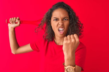 Tenis raketi tutan Brezilyalı genç sporcu. Kırmızı arka planda duruyor. Sinirli ve sinirli bir şekilde bağırıyor.