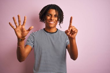 Rastalı Afro adam, donanma çizgili tişört giyiyor. İzole edilmiş pembe arka plan üzerinde duruyor. Altı numarayı işaret ediyor..