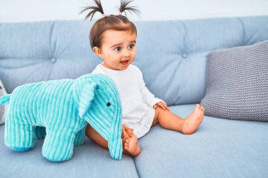 Anaokulunda kanepedeki renkli oyuncakların yanında mutlu bir bebek.