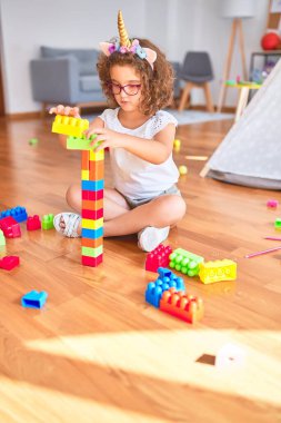 Gözlük takan ve tek boynuzlu at diademi takan güzel çocuk anaokulunda yapı taşlarıyla oynuyor.