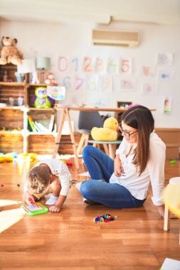 Anaokulundaki bir sürü oyuncağın etrafında dijital tahta kullanarak güzel öğretmen ve bebek çizimi yapıyorlar.