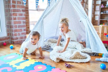 Anaokulundaki bir sürü oyuncağın etrafında battaniyenin üstünde oynayan güzel bebekler.