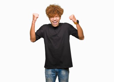 Çok mutlu ve heyecanlı kaldırdı, silah ile kazanan jest yapıyor gülümseyen ve başarı için çığlık siyah t-shirt giyen afro saçlı Genç yakışıklı adam. Kutlama kavramı.