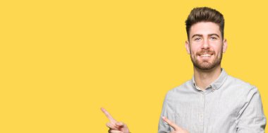 Genç, yakışıklı, rahat gömlekli, gülümseyen ve kameraya bakan, iki elini ve parmağını yan tarafa doğru gösteren bir adam..