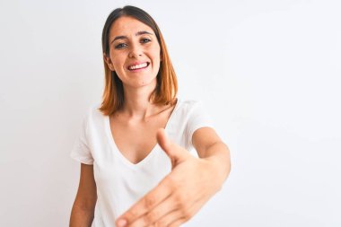Güzel kızıl saçlı kadın, izole edilmiş arka planda günlük beyaz tişört giyip dostça gülümseyerek selamlaşma ve selamlama sunuyor. Başarılı bir iş..
