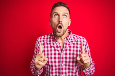 Genç, yakışıklı bir adam, izole edilmiş arka planda şaşkın şaşkın yukarı bakıyor, parmaklarıyla işaret ediyor ve kollarını kaldırıyordu..