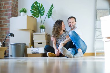 Orta yaş üst düzey romantik çift etrafında karton kutular ile daire katında oturan ve yeni bir eve taşınmak için mutlu gülümseyen aşk
