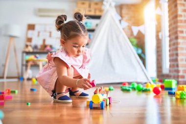 Genç, güzel bir çocuk yerde oturmuş anaokulunda tahta tren oyuncağıyla oynuyor.
