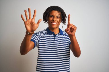 Sarı çizgili mavi polo giyen Afro bir adam izole edilmiş beyaz arka planda duruyor ve altı numarayı işaret ediyor kendinden emin ve mutlu gülümserken..