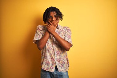 Tatilde sarı arka planda çiçekli gömlek giyen Afro bir adam ağzını yanlışlıkla ellerle kapatarak şok etti. Gizli konsept.