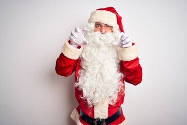 Middle age handsome man wearing Santa costume standing over isolated white background smiling funny doing claw gesture as cat, aggressive and sexy expression
