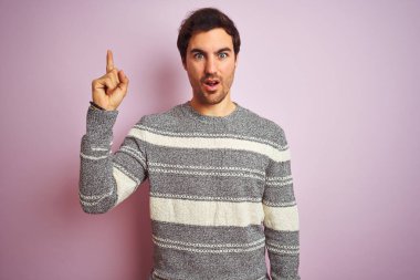 İzole edilmiş pembe arka planda duran sıradan çizgili süveter giyen genç yakışıklı adam başarılı bir fikirle parmağını kaldırdı. Heyecanlı ve mutlu. Bir numara..