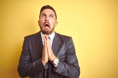 Sarı arka plan üzerinde genç yakışıklı bir iş adamı. Yüzünde umut ifadesi olan çok duygusal ve endişeli ellerle yalvarıyor ve dua ediyor. Af diliyor. Din kavramı.