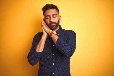 Genç, yakışıklı Hintli iş adamı, izole edilmiş sarı arka plan üzerinde gömlek giyiyor. Uyuyor, yorgun düşler görüyor ve elleri ile birlikte poz veriyor, gözleri kapalı gülümsüyor..