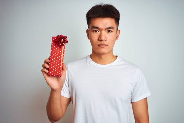 Sevgililer günü kartı tutan Asyalı genç bir adam izole edilmiş beyaz arka planda duruyor. Akıllı yüzünde kendine güvenen bir ifade var ve ciddi düşünüyor.
