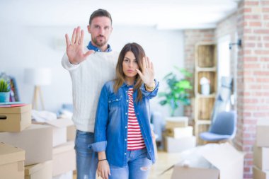 Genç ve güzel bir çift, yeni evlerinde karton kutuların etrafında durmuş avuç içiyle şarkı söylemeyi kesiyorlar. Yüzünde olumsuz ve ciddi bir jest olan uyarı ifadesi.