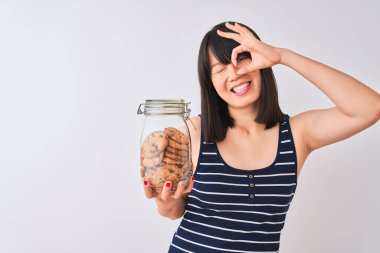 Genç, güzel bir Çinli kadın, izole edilmiş beyaz arka planda elinde kurabiye kavanozuyla gülümseyen bir gülümseme ile el pençe divan duruyor.