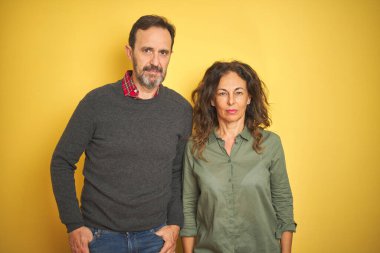 Soyutlanmış sarı arka planda güzel bir orta yaşlı çift. Yüzlerinde ciddi bir ifadeyle rahatlamış. Basit ve doğal bir şekilde kameraya bakıyorsun..