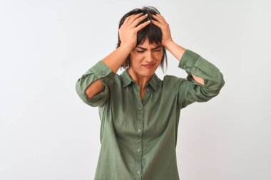 Yeşil gömlekli genç bir kadın, izole edilmiş beyaz arka planda dikilip acı ve migren yüzünden çaresiz ve stresli bir şekilde acı çekiyor. Ellerini başının üstüne koy..