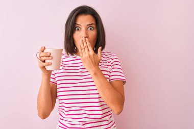 Genç ve güzel bir kadın, izole edilmiş pembe arka plan örtüsünün başında dikilip kahve içiyor. Ağzı kapalı, utancından ağzı açık, korku ifadesi, sessizlikten korkmak, gizli bir konsept.
