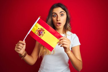 İspanyol bayrağını kırmızı arka planda tutan genç ve güzel bir kadın. Şaşırmış bir yüzle korkmuş, korku ifadesinden korkmuş ve heyecanlanmış.