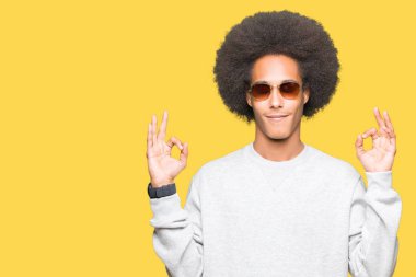 Güneş gözlüğü takıyor afro saçlı genç Afro-Amerikan adam sakin ol ve gülümseyen gözlerle kapalı parmak jestle meditasyon yapıyor. Yoga kavramı.