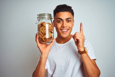 Genç Brezilyalı adam izole edilmiş beyaz arka planda duran bir kavanoz kurabiyeyi tutarken bir fikir ya da soru işareti ile şaşırdı.